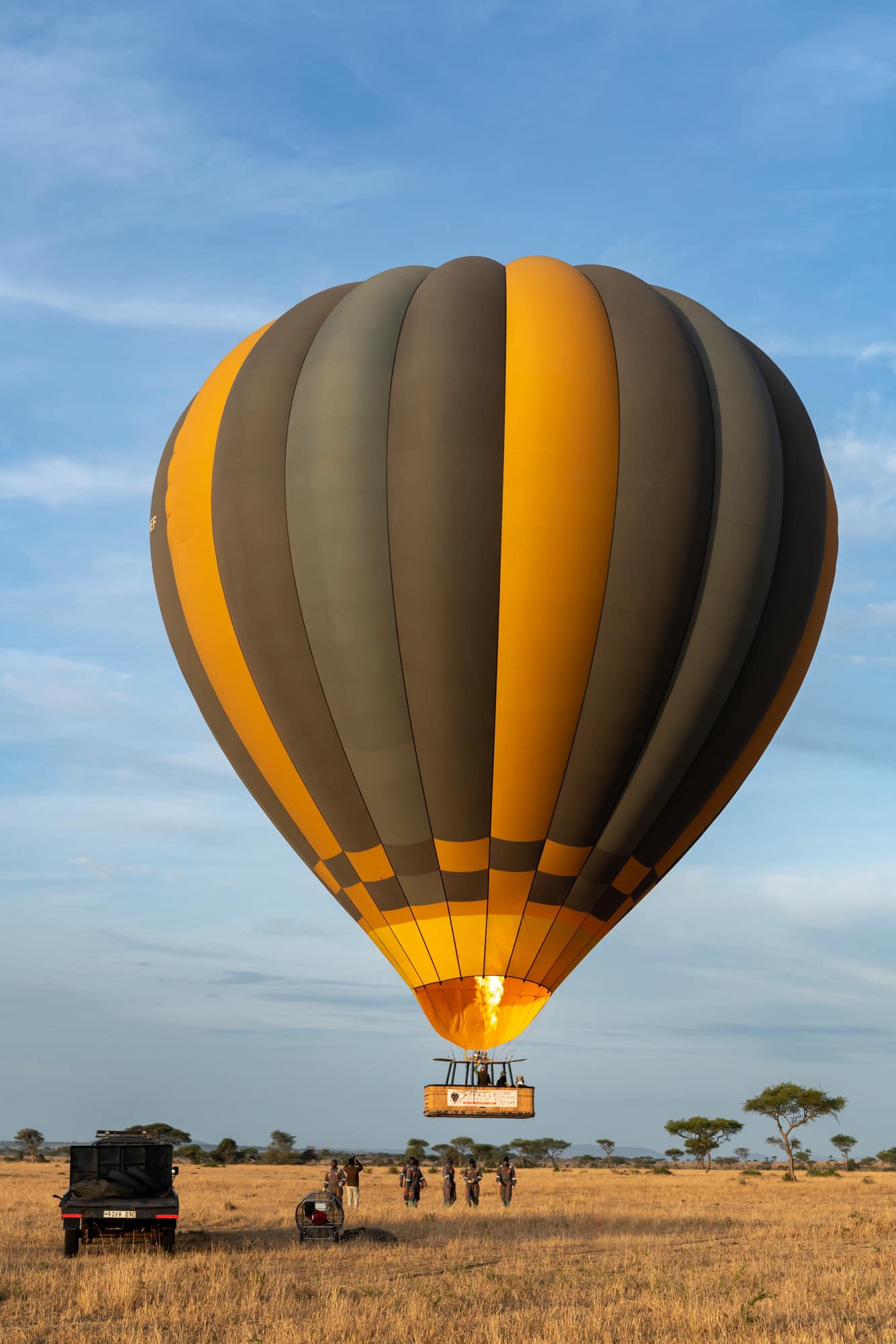 Hot air balloon over the savannah with safari vehicles below