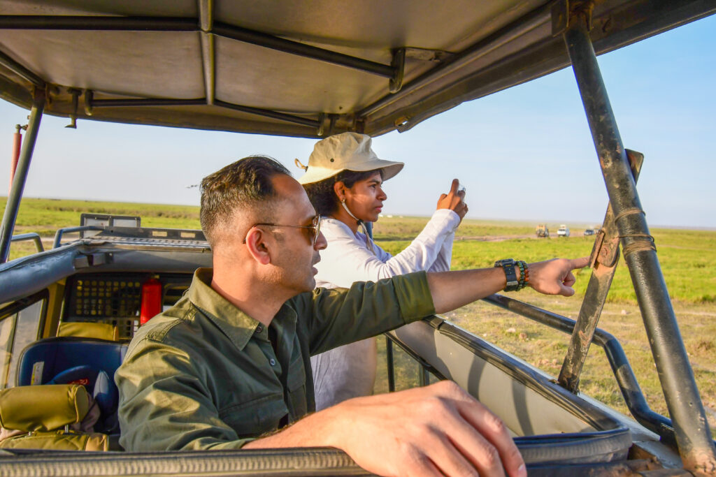 Two guests photographing wildlife from an open safari vehicle